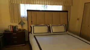 A neatly made bed with a headboard, a bedside table with books, a lamp, and a window with curtains. - Lake View Home Walking Distance to Town and Vin du Lac Winery (Chelan)