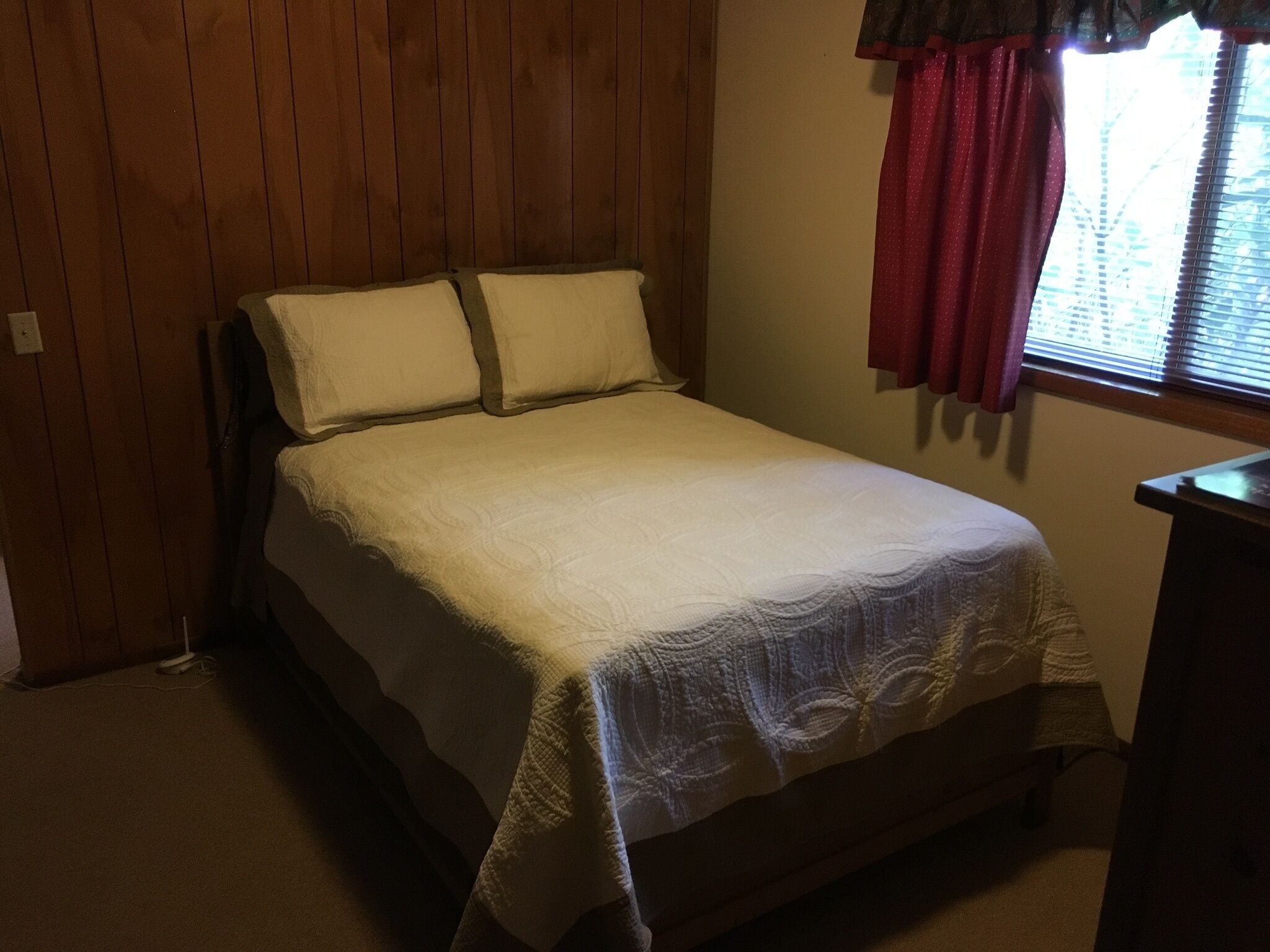Une chambre à coucher avec un lit, des murs en bois, une fenêtre avec des stores et un rideau rouge.