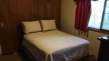 Une chambre à coucher avec un lit, des murs en bois, une fenêtre avec des stores et un rideau rouge.