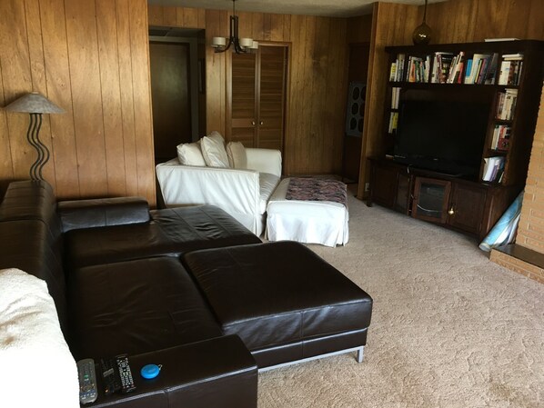 A living room with a brown leather sofa, a white sofa, a bookshelf, and a television.