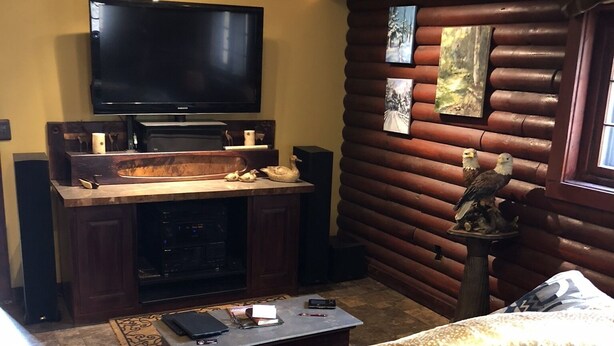 A cozy living room with a flat-screen TV, wooden log wall, leather sofa, and a coffee table. - Little Manistee River Cabin (Irons)