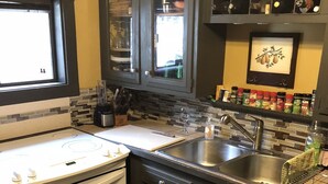 A compact kitchen with a stove, oven, sink, and a spice rack. - Little Manistee River Cabin (Irons)