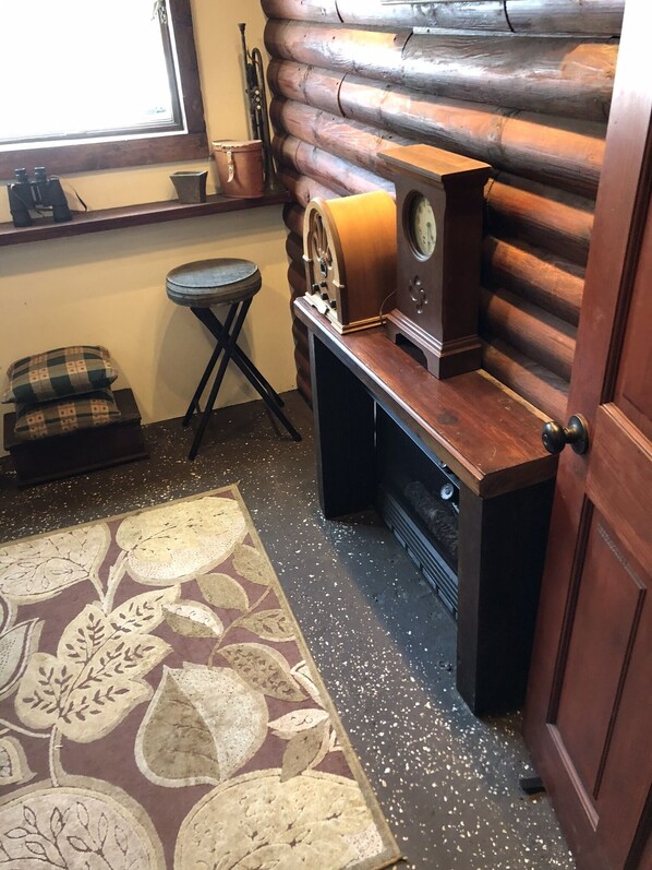 Interior de uma cabana de tronco com um banco de madeira, uma mesa pequena e um tapete estampado.
