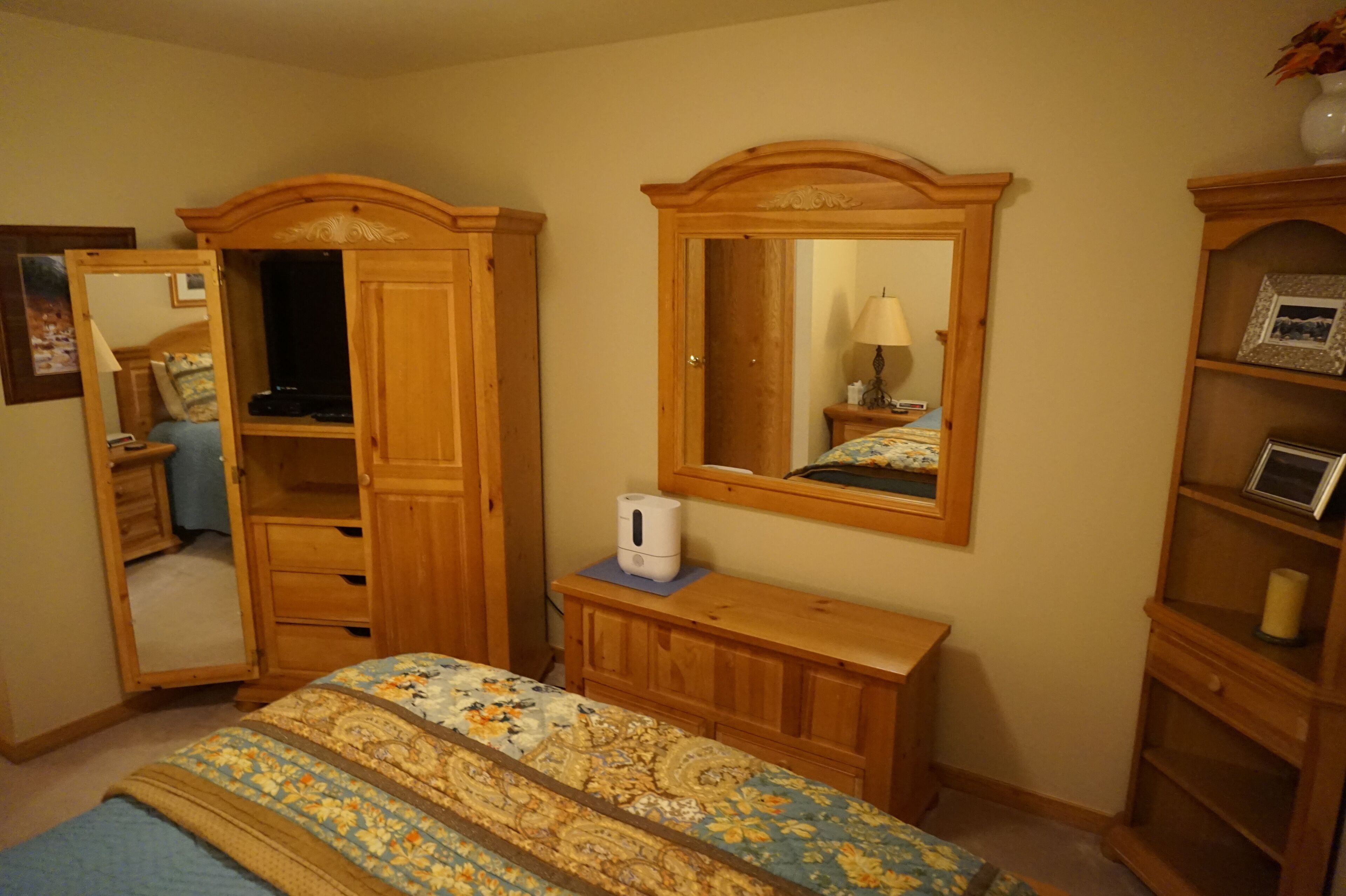 Une chambre à coucher avec un lit, une armoire en bois, un miroir et une petite table avec une lampe.