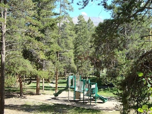 Explore a natural playground with a slide and climbing structures for kids, set amidst a serene forest.