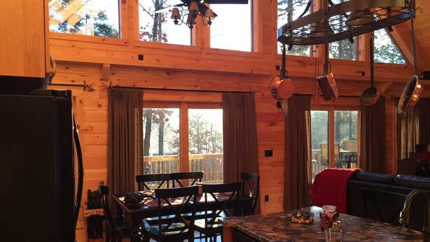 Ein Interieur einer Holzhütte mit Küche, Essbereich und großen Fenstern.