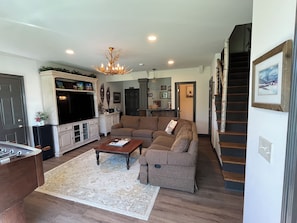 A living room with a sectional sofa, a flat-screen TV, a wooden coffee table, and a chandelier.