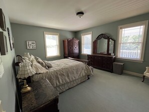 A bedroom with a bed, dresser, mirror, and two windows.