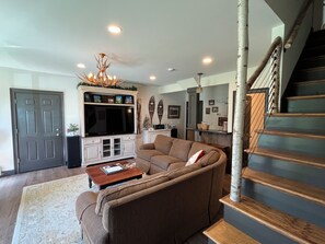 A living room with a sectional sofa, a flat-screen TV, a coffee table, and a staircase with wooden steps.
