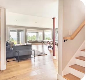 A spacious living room with a grey sofa, a coffee table, and a view of the outdoors through large windows. - Wine country with views (Newberg)