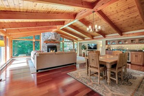 A spacious living area with a fireplace, a dining table, and a kitchen in the background. - Quechee House with Hot Tub, Sauna & Club Access (Quechee)