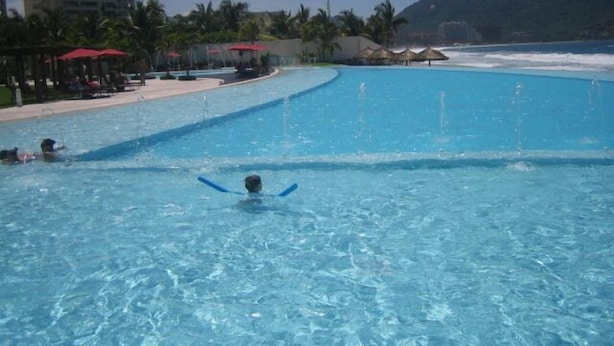 Een groot zwembad met helderblauw water, omringd door een strand en palmbomen.