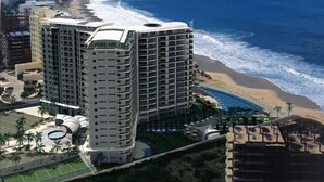 Een kusthotel met meerdere hoge gebouwen, een strand en een bergachtige achtergrond.