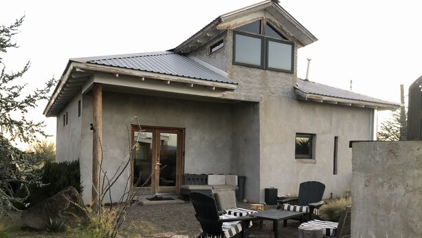 Une maison moderne avec une façade en pierre, une grande porte vitrée et un patio aménagé avec du mobilier d’extérieur.