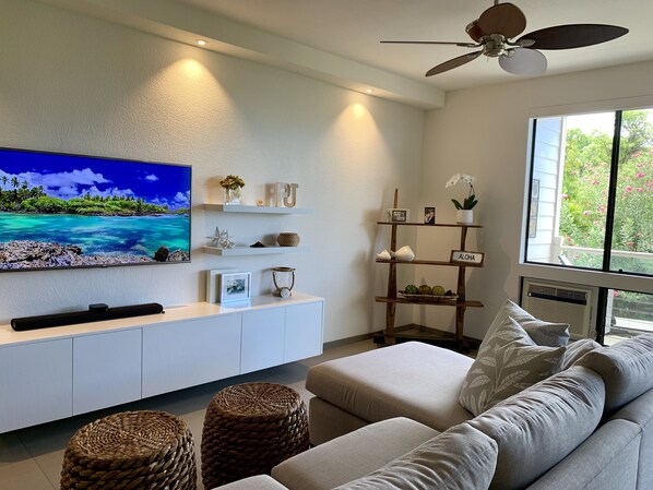 Uma sala de estar moderna com televisão de tela plana, ventilador de teto e uma janela grande com vista para o verde.