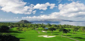 A golf course with a water body and a mountain in the background.