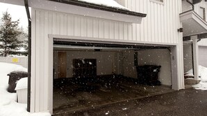 A garage with a partially open door, snow on the ground, and a snow-covered tree in the background. - PRL3 by Park City Experience - Ultimate convenience near Deer Valley and Main St (Park City)