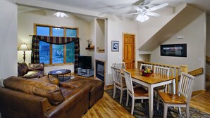 A cozy living room with a brown leather sofa, a television, and a fireplace. There's a dining area with a wooden table and chairs, and a ceiling fan above. - PRL3 by Park City Experience - Ultimate convenience near Deer Valley and Main St (Park City)