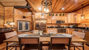 L’intérieur d’un chalet en bois chaleureux et accueillant, avec une table à manger dressée pour quatre personnes, une cuisine équipée d’appareils modernes et un panneau indiquant que l’on se trouve dans une zone où vivent des ours.