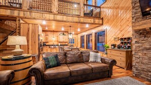 Un intérieur de chalet chaleureux avec un canapé en cuir, un plancher en bois, une cuisine et un coin repas.