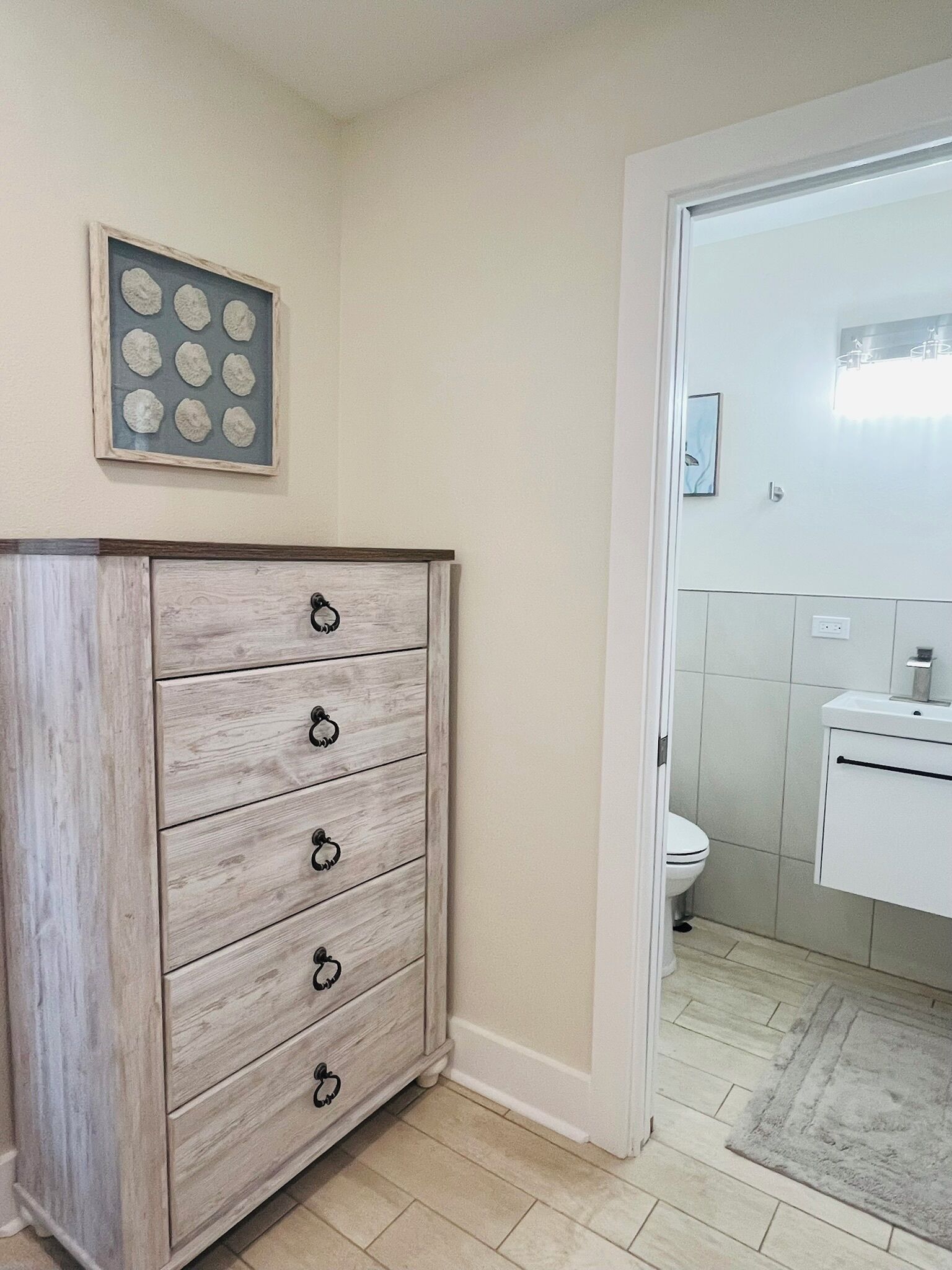 A bathroom with a wooden dresser, a framed picture, and a white sink.
