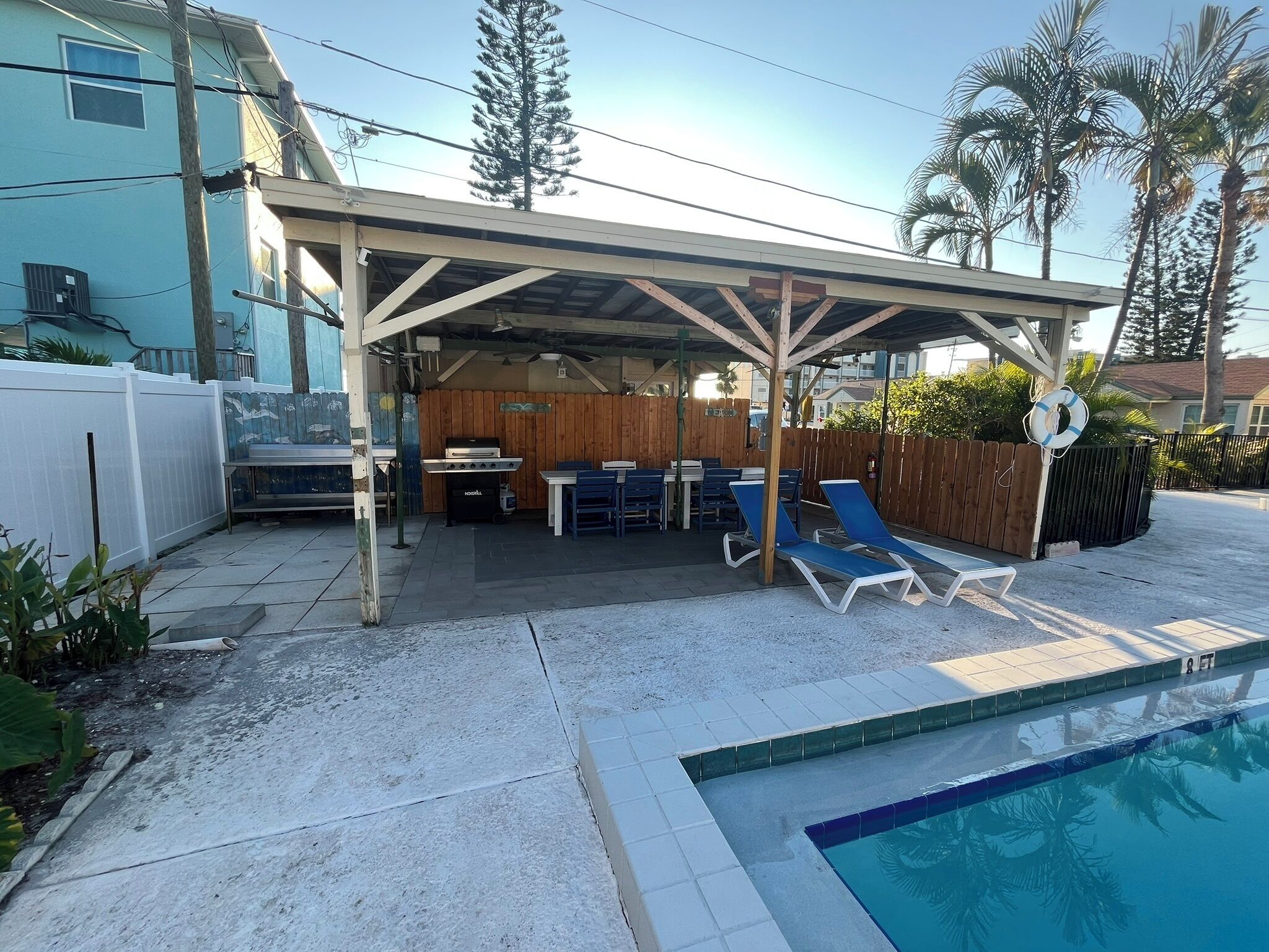 Un patio exterior techado con piscina, zona de estar y parrilla.