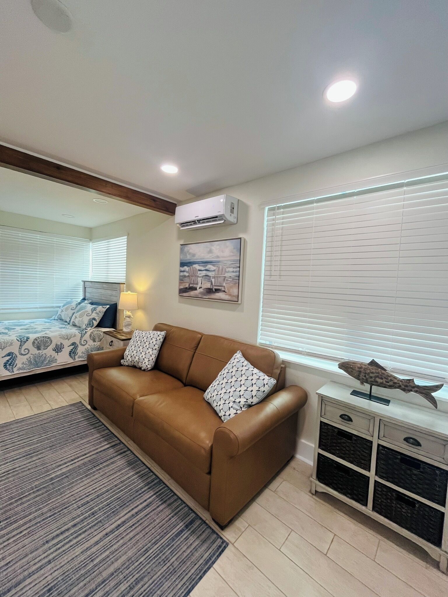 A modern living room with a brown leather sofa, a patterned rug, a small side table with a lamp, and a fish decoration on a cabinet.