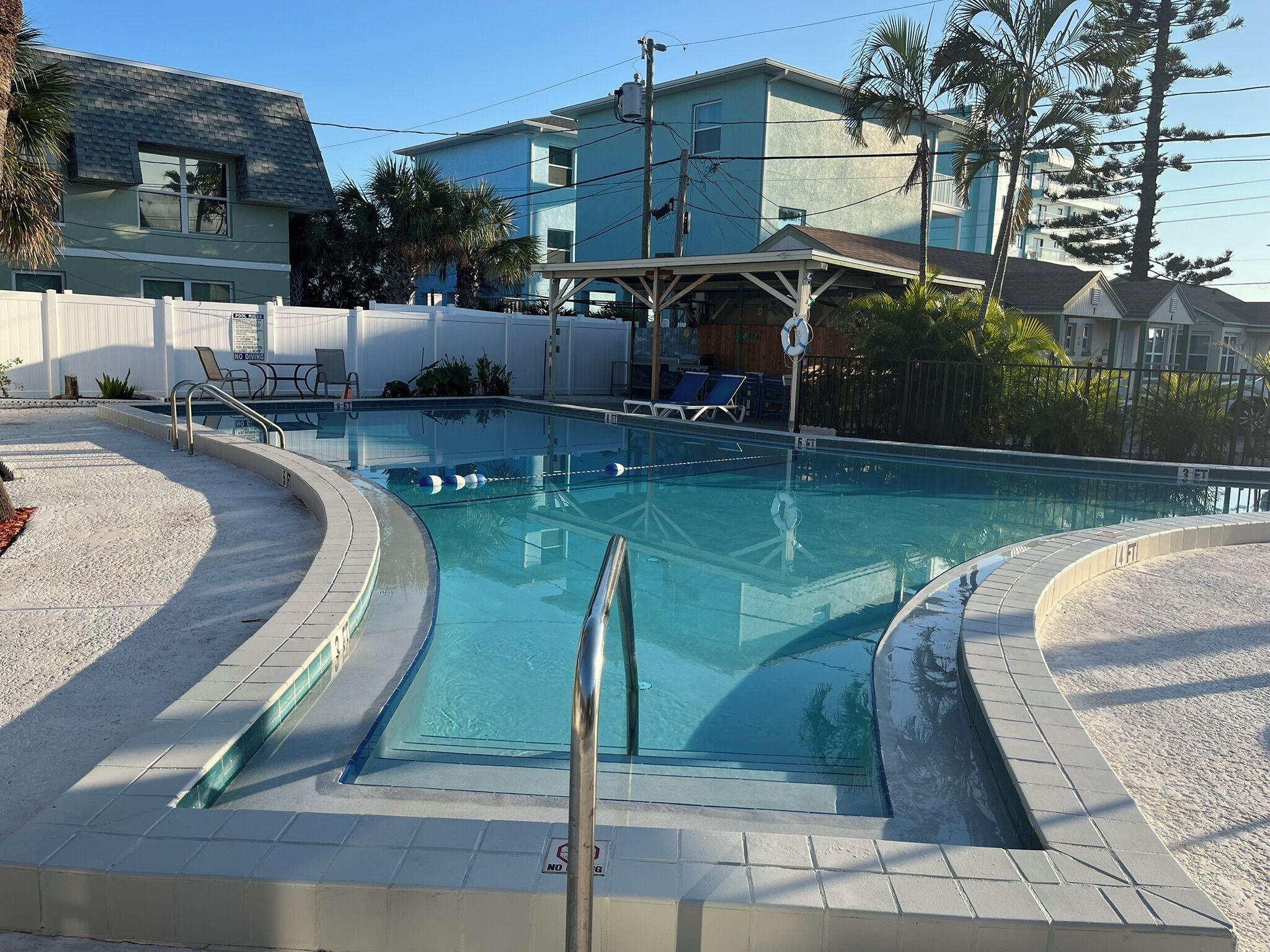 A swimming pool with a tiled deck, lounge chairs, and a covered area with a roof.