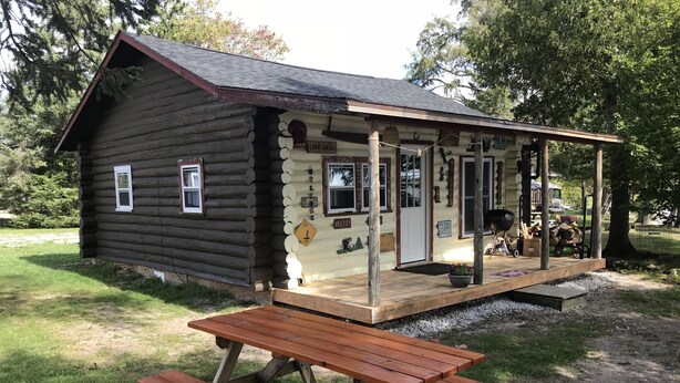 A rustic log cabin with a porch and a picnic table in front. - Cabin #5 On Beautiful Brevort Lake (Moran)