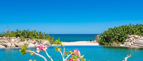 A clear blue pool with a view of the ocean and a sandy beach.