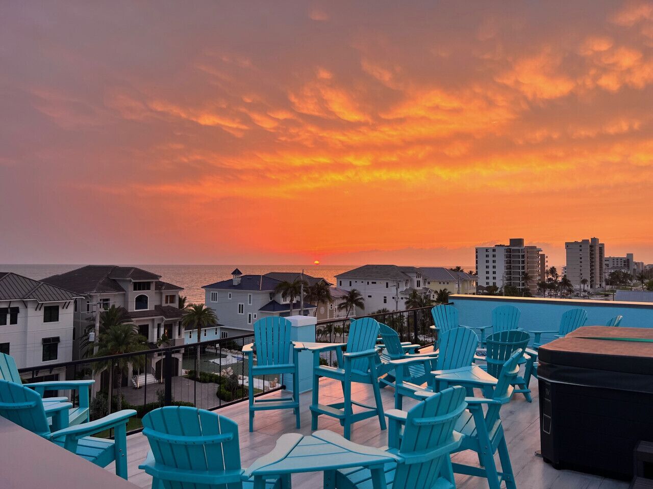 Una terraza en la azotea con sillas azules y vistas a la puesta de sol sobre el océano.