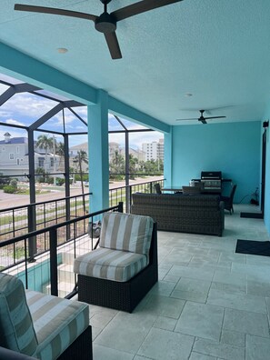 Un espacio al aire libre techado con mobiliario de mimbre, ventiladores de techo y vistas del barrio circundante.