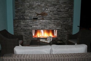 Una habitación con chimenea de piedra, muebles de mimbre y una pequeña mesa con copas de vino.