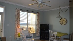 Un salon avec un ventilateur de plafond, un téléviseur, une table à manger avec des chaises et une horloge au mur.