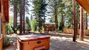 Un jacuzzi de madera con escalones, rodeado de altos árboles y una terraza de madera.
