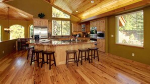 Una cocina amplia con pisos de madera, una isla central con taburetes y grandes ventanales con vistas al exterior.
