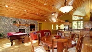 Un comedor amplio con mesa y sillas de madera, mesa de billar y pared de piedra.