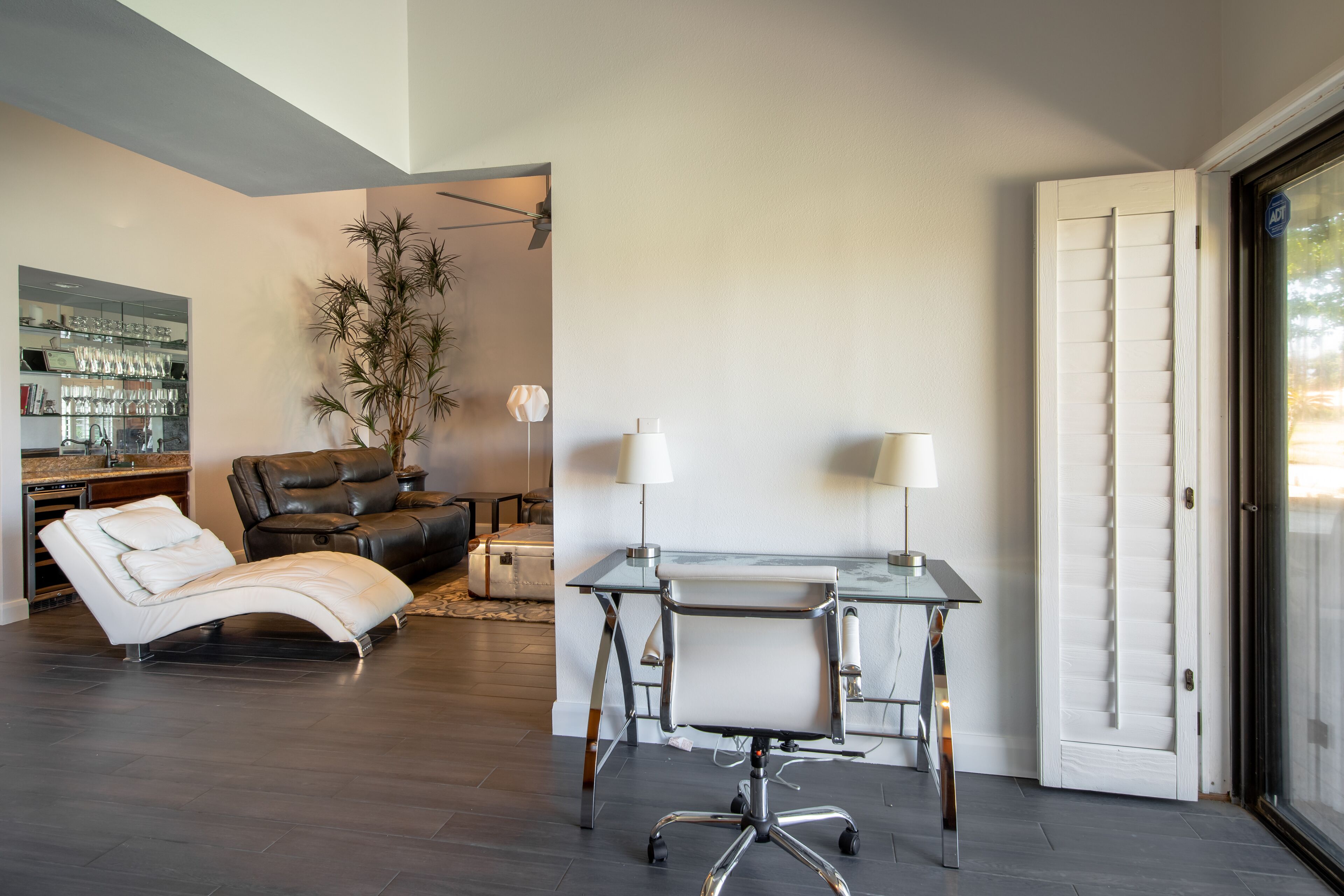 A modern living room with a glass desk, leather sofa, and a dining area with a bar.