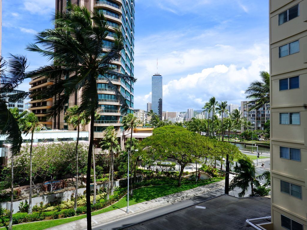 Un edificio alto dal design moderno, circondato da palme e un curato giardino.