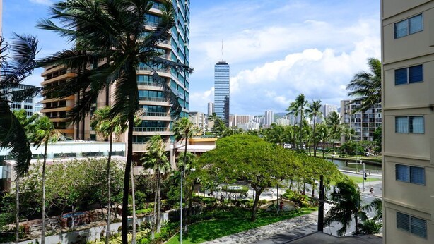 Un edificio de gran altura con diseño moderno, rodeado de palmeras y un jardín bien cuidado.