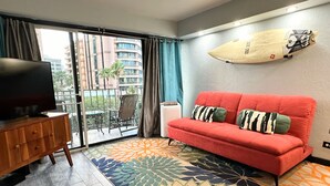 Una sala de estar con un sofá rojo, un televisor sobre un mueble de madera, una alfombra colorida y una tabla de surf en la pared.
