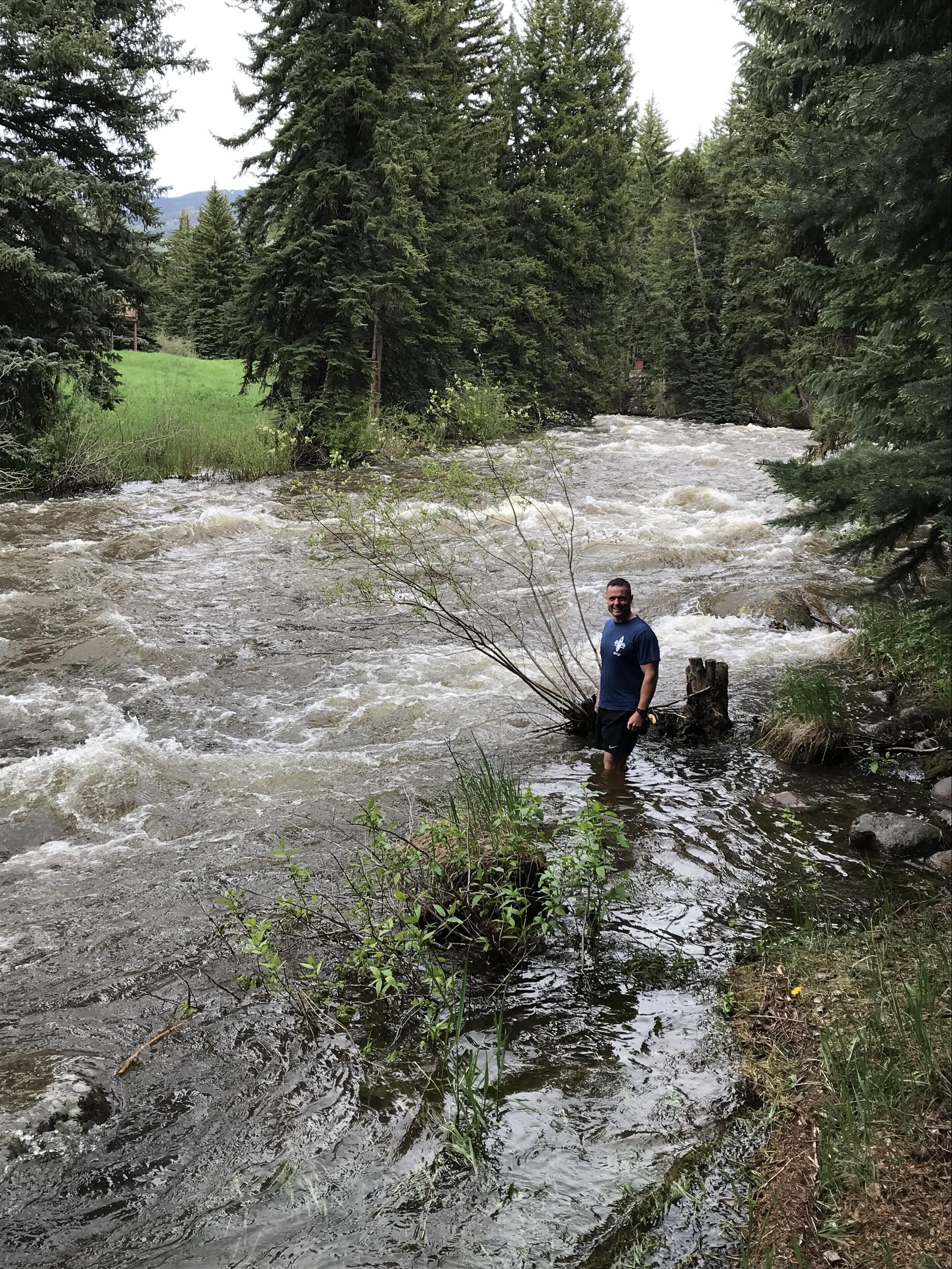 Eine Person steht in einem Fluss, umgeben von dichtem Wald.
