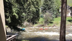 A river with a kayaker, surrounded by trees and a building in the background. - Gore Creek just off the back deck, Free Bus, Wi-Fi, Hot Tub, Summer Pool (Vail)