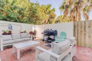 Une terrasse extérieure équipée d’un barbecue, d’un coin salon et de plantes en pot.