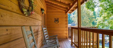 Een houten veranda met schommelstoelen, een houten muur met een krans, en uitzicht op bomen.