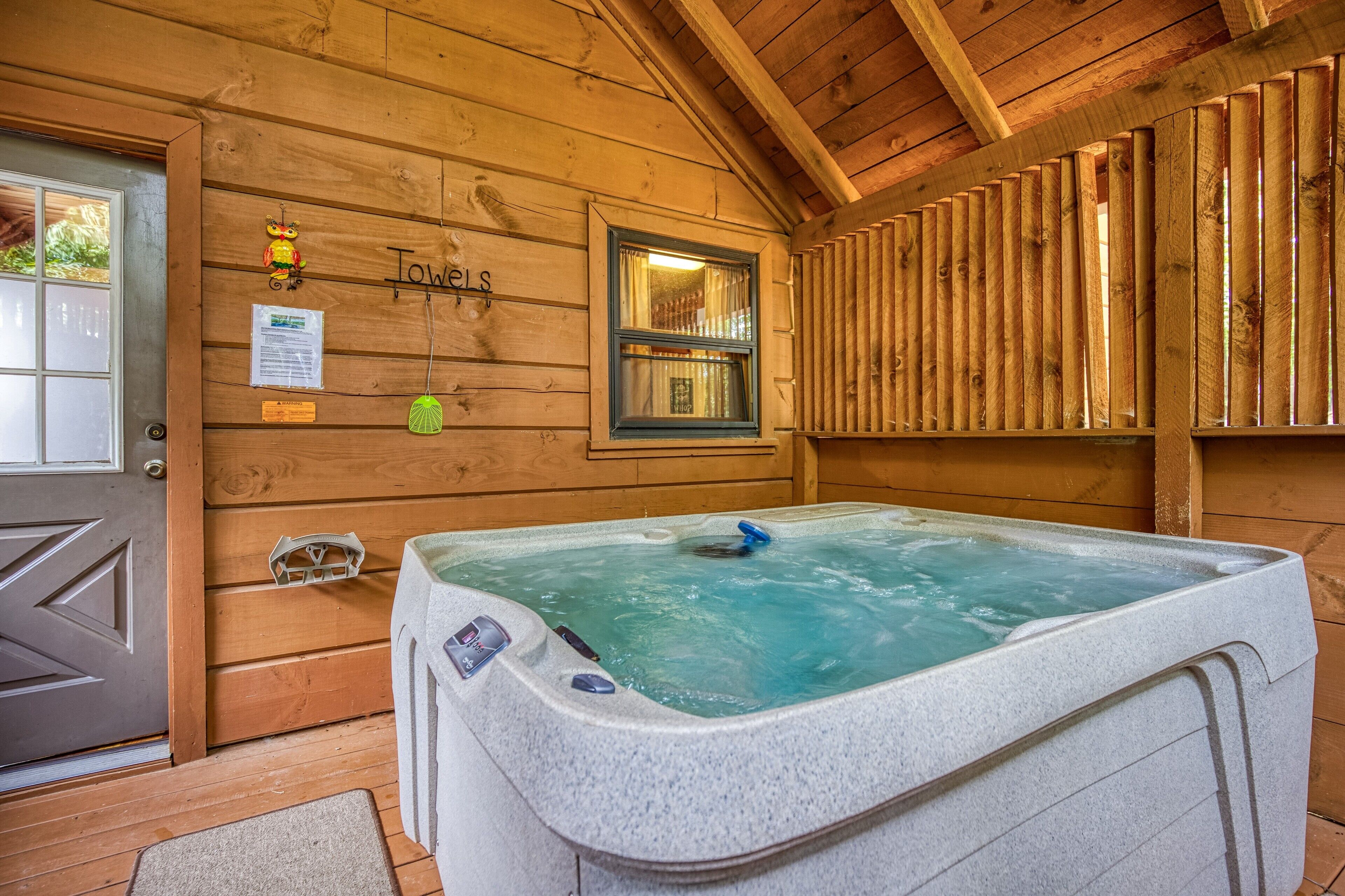A wooden cabin interior with a hot tub, wooden walls, a window, and a door.