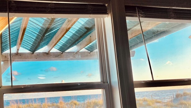 A room with a view of the beach, a wooden deck, and a window with a view of the ocean. - 10% off weeklong  stays booked now. Clean & charming oceanfront  home with view (Oak Island)