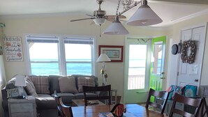 A cozy living room with a wooden dining table, chairs, a sofa, and a ceiling fan. - 10% off weeklong  stays booked now. Clean & charming oceanfront  home with view (Oak Island)