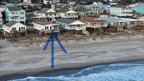 A coastal residential area with houses on stilts, a sandy beach, and ocean waves. - 10% off weeklong  stays booked now. Clean & charming oceanfront  home with view (Oak Island)
