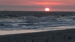 A sunset over the ocean with a sandy beach and a fence in the foreground. - 10% off weeklong  stays booked now. Clean & charming oceanfront  home with view (Oak Island)